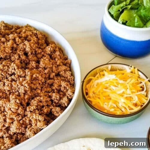 A bowl of taco meat with taco toppings nearby.