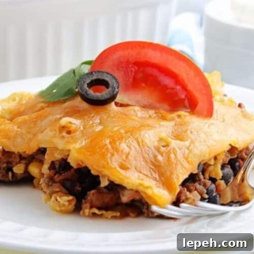 A slice of walking taco casserole on a plate, with olives and tomatoes on top.