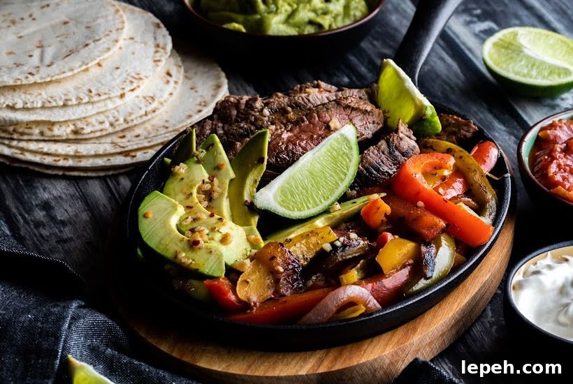 Skillet filled with steak, lime wedges and sliced vegetables with a stack of tortillas.