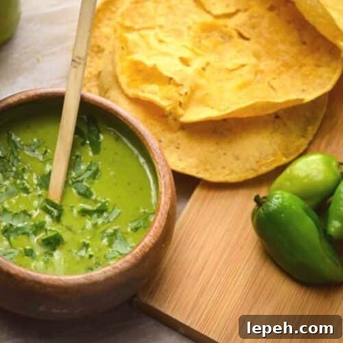 A bowl of homemade tomatillo hot sauce with tortillas near.