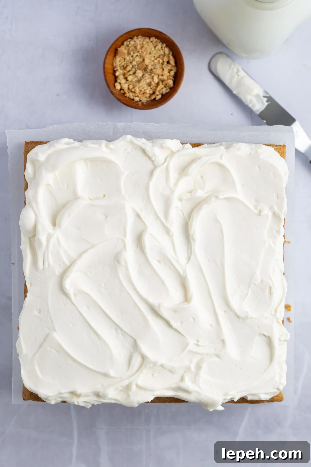 frosting topping swirled on top of cake with a bowl of graham cracker crumbs