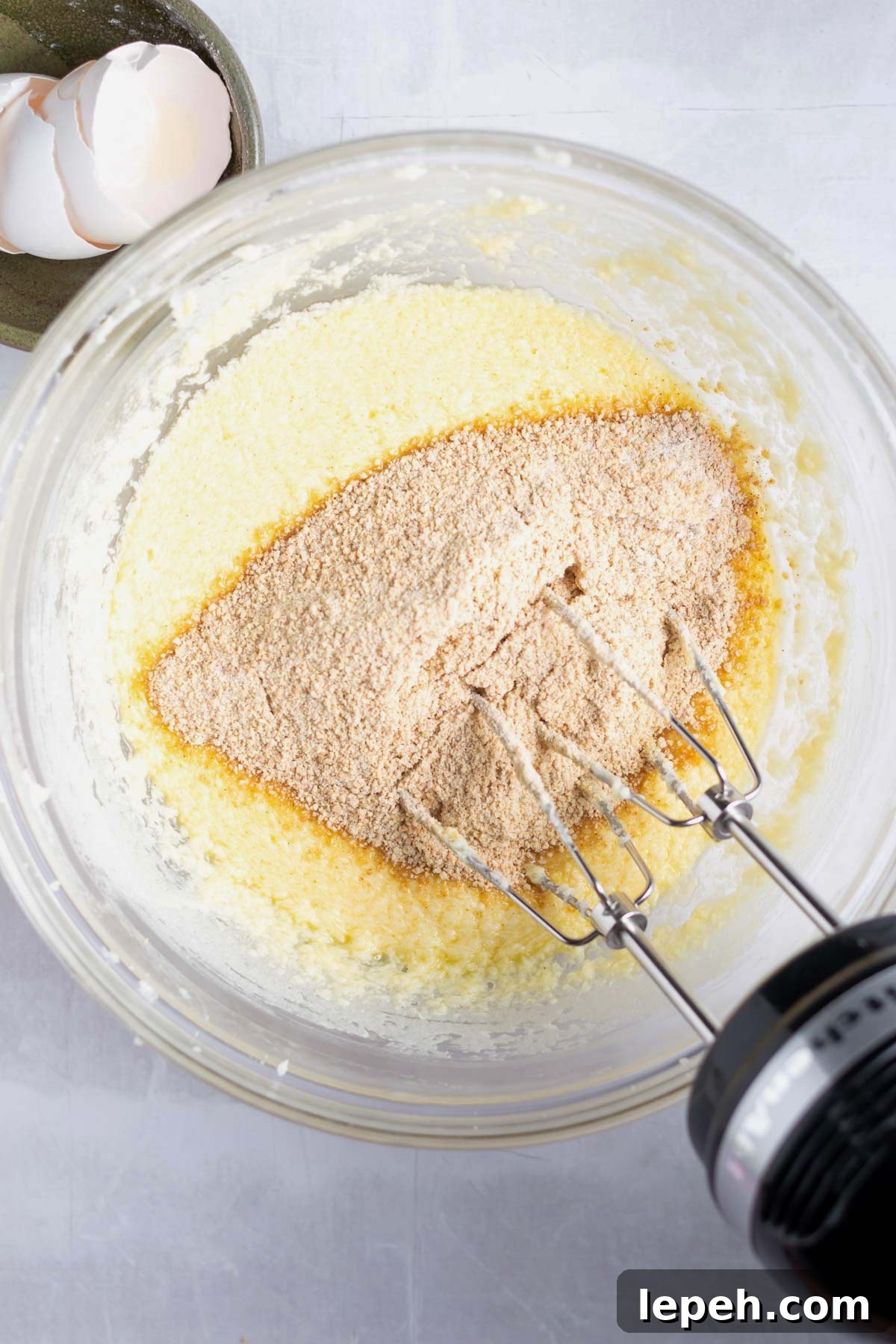 dry ingredients being added to wet ingredients in a bowl with a hand mixer