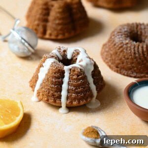 Mini mace bundt cake with white glaze on an orange surface.