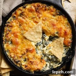 Golden-brown spinach artichoke dip in skillet with tortilla chips.
