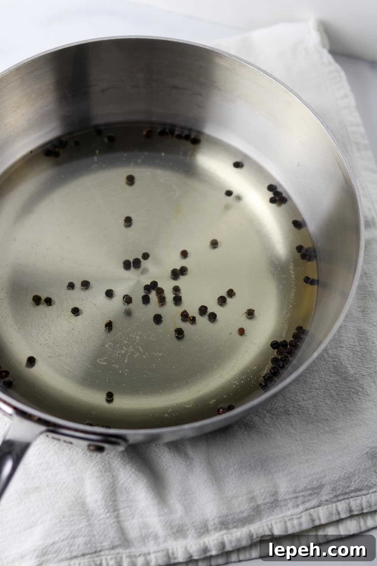 A saucepan filled with water and whole peppercorns on a white kitchen towel.