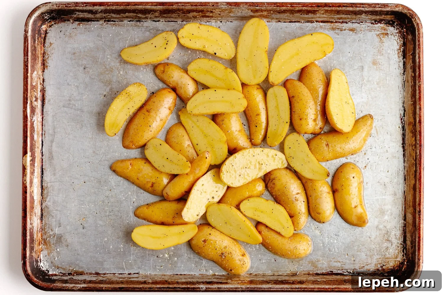 Halved fingerling potatoes on a baking sheet tossed with avocado oil, salt and pepper for roasting.