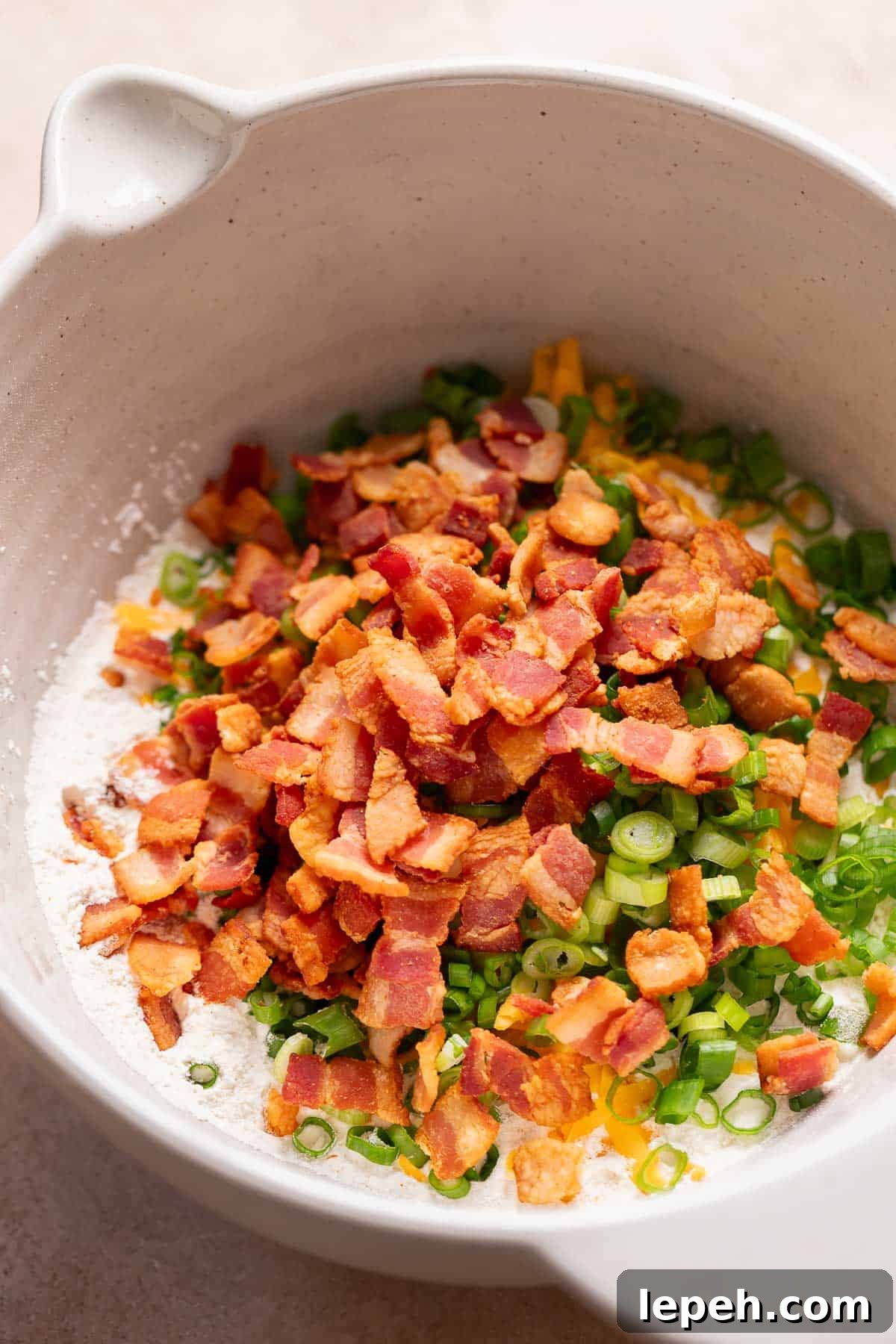 A mixing bowl with the dry ingredients, bacon, cheese, and scallions before mixing.
