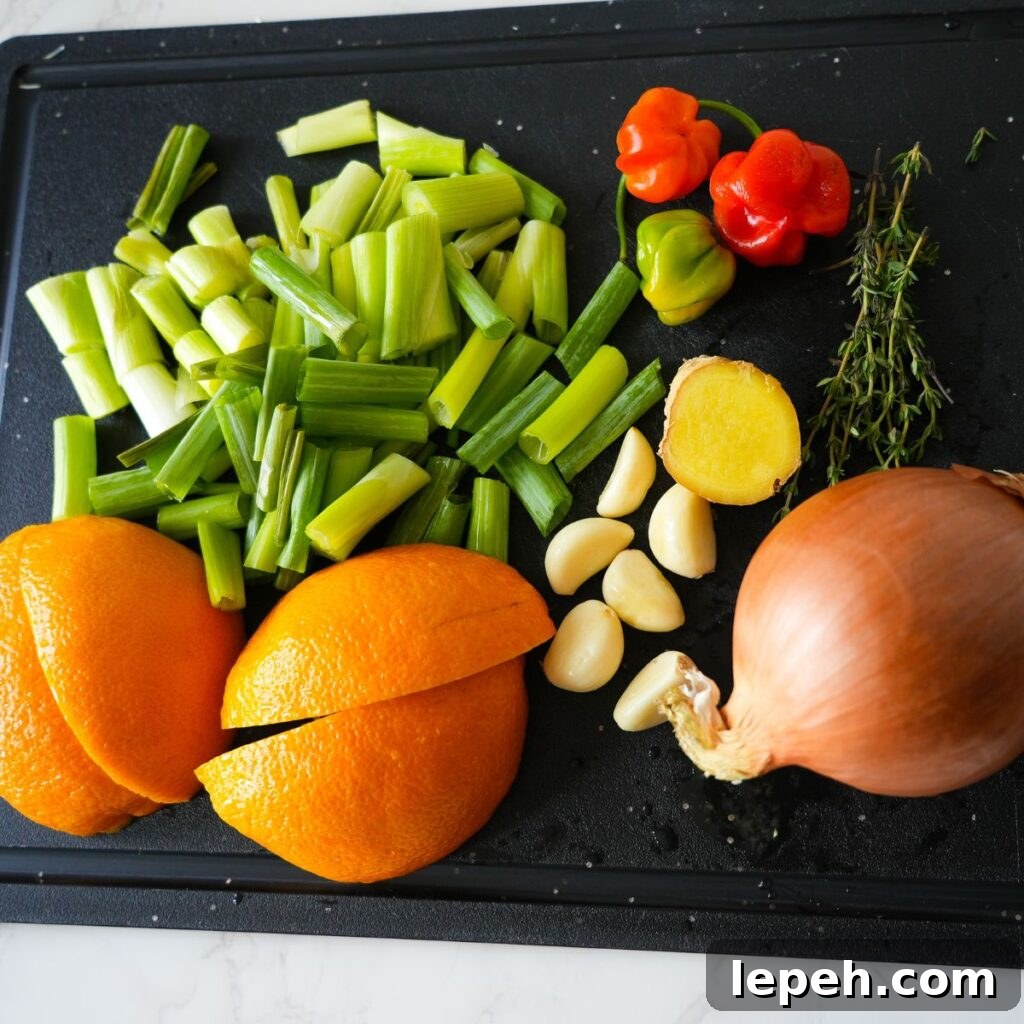 Chopped oranges, garlic, scallions, thyme, ginger and scotch bonnet peppers on a cutting board.