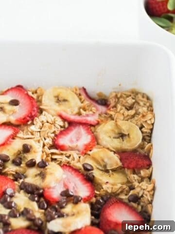 Banana baked oatmeal with strawberries and chocolate chips in a white baking dish.