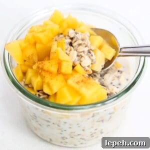 Overnight oats topped with pieces of fresh mango and a spoon.