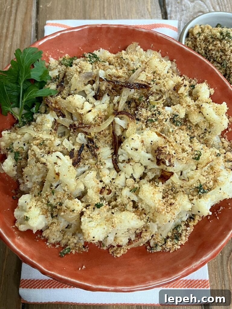 Smashed Sauteed Cauliflower with Pangrattato (Breadcrumbs) on orange serving dish with parsley garnish and more bread crumbs in back ground.