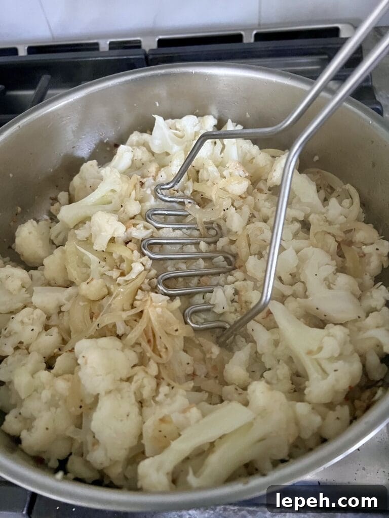 Mashing cauliflower in skillet with potato masher.