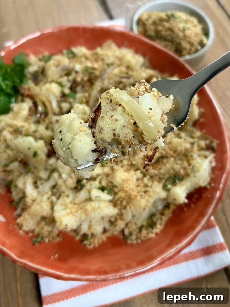 Close up of smashed sauteed Italian cauliflower on fork with plate of it and extra pangrattato in background.