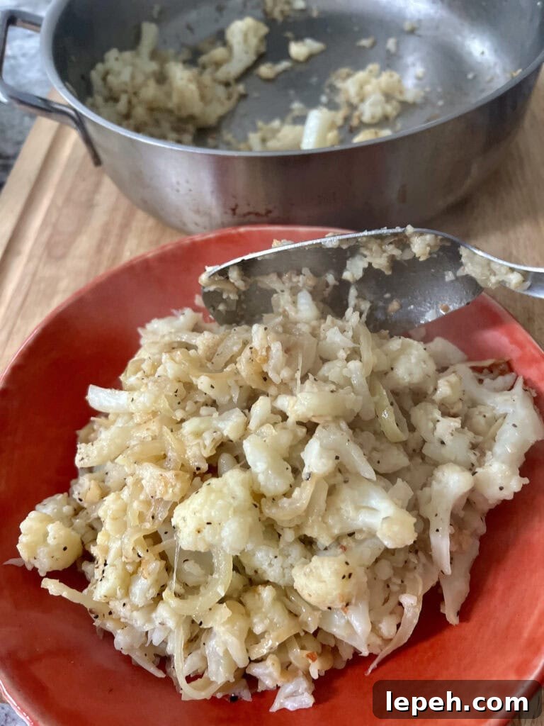 Transferring Italian Smashed Sauteed Cauliflower from pan to orange serving dish with spoon.