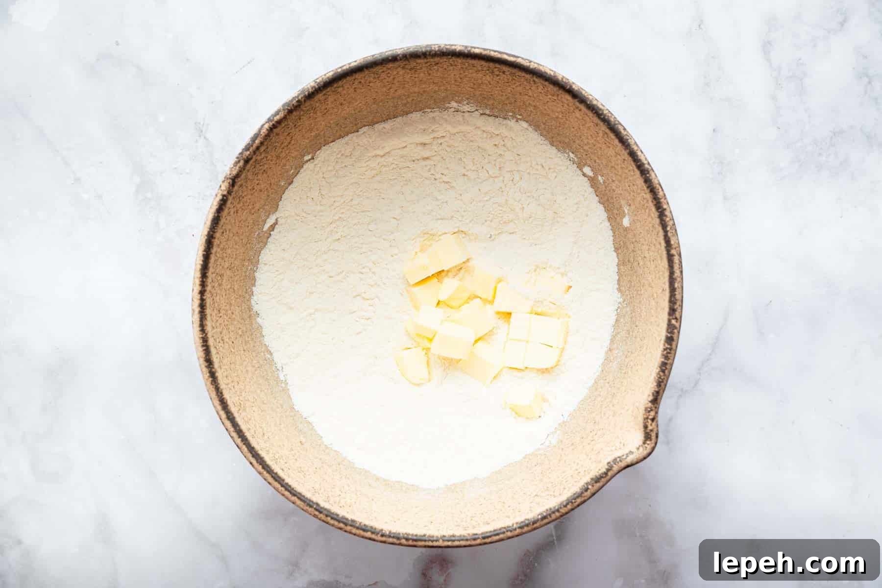 Brown pottery bowl with flour mixture and diced butter in center.