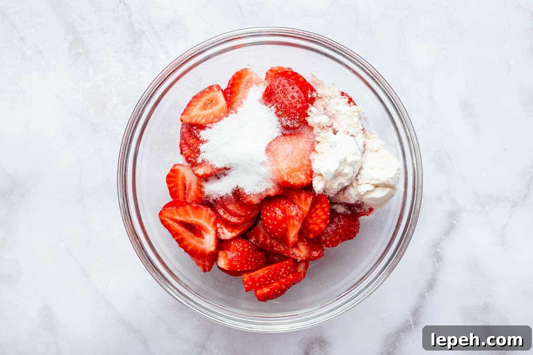 Glass bowl with sliced strawberries with flour and sugar on top.