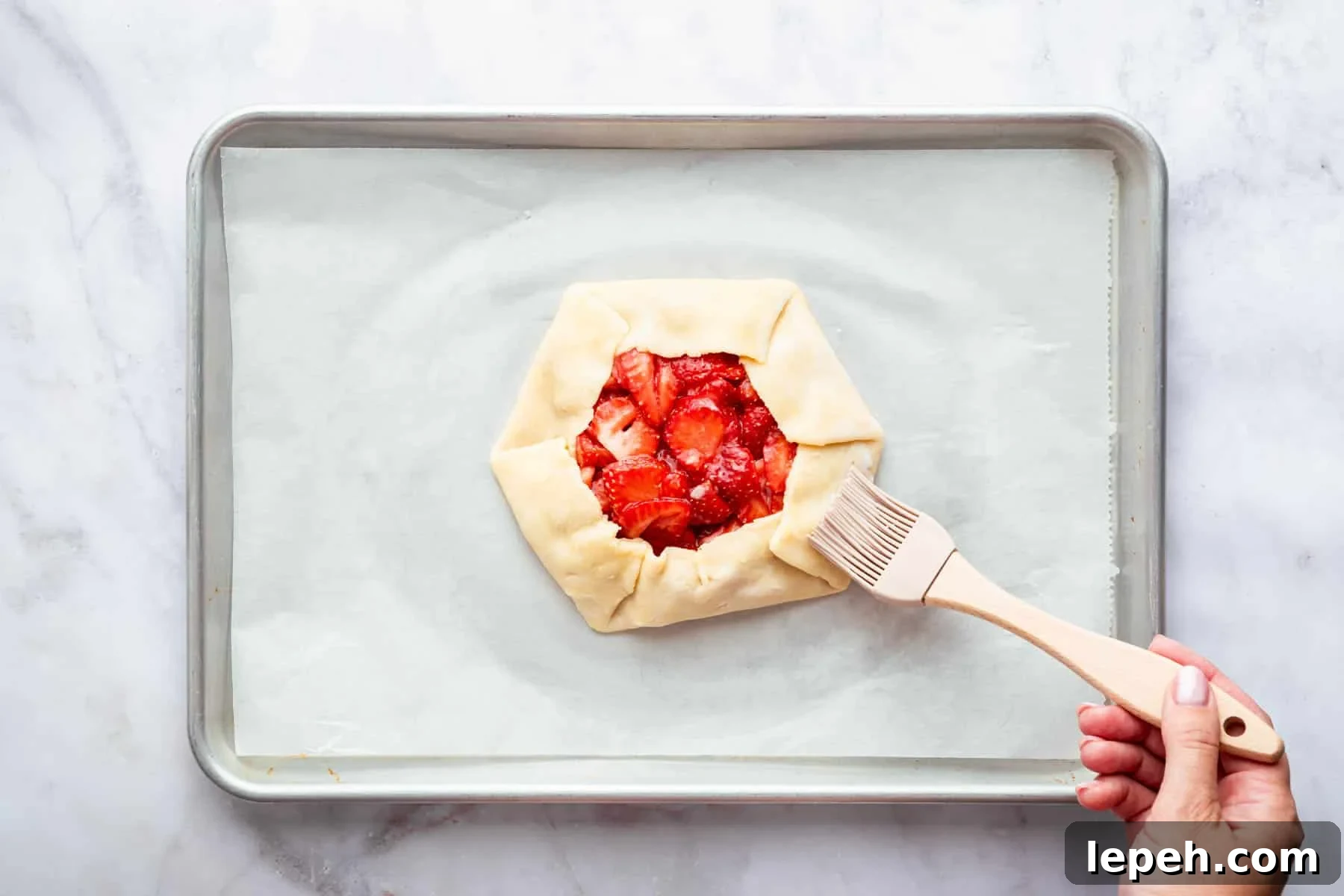 Hand brushing milk on pastry crust with berries in center.