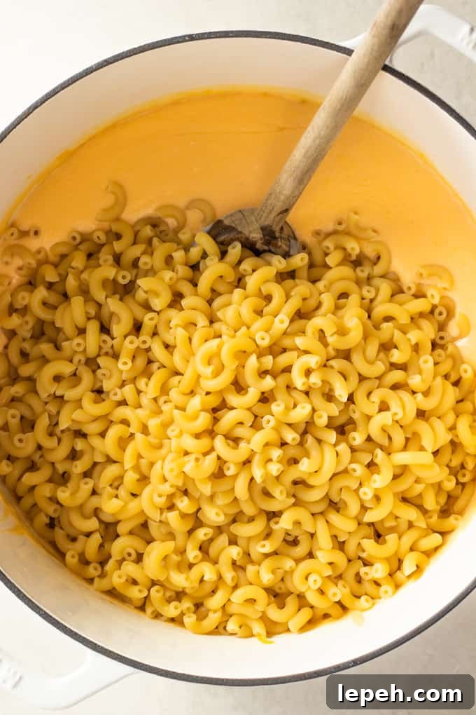 Elbow macaroni noodles added to a large dutch oven of homemade cheese sauce for macaroni and cheese.