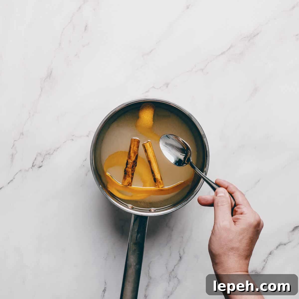 stirring a sugar syrup in a pot with cinnamon and orange peel.