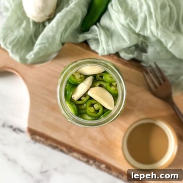 Pickled serrano peppers in a jar surrounded by garlic and peppers.