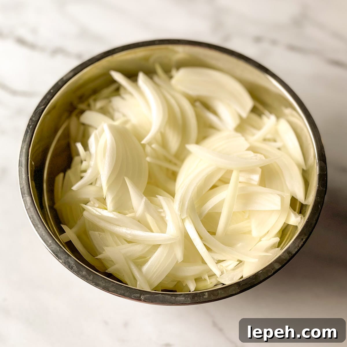 Sliced onions sit in a metal bowl.