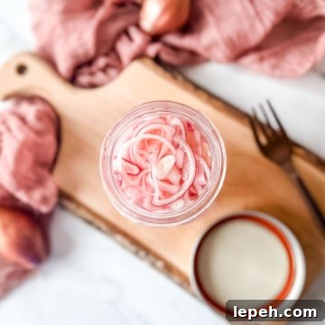 Quick pickled shallots in a glass jar on a rustic wooden cutting board.