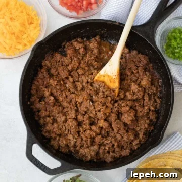 Taco meat in a cast iron pan with fixings for tacos around it.