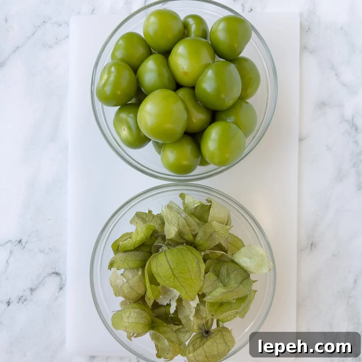 two bowls on the counter, one with peeled green tomatillos and the other with the husks. 