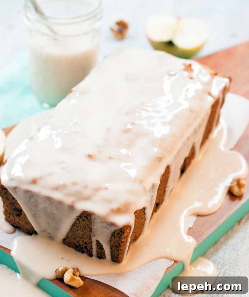 Vertical image of a loaf-shaped cake with sugar icing poured on top and running all over the parchment paper and board beneath it.