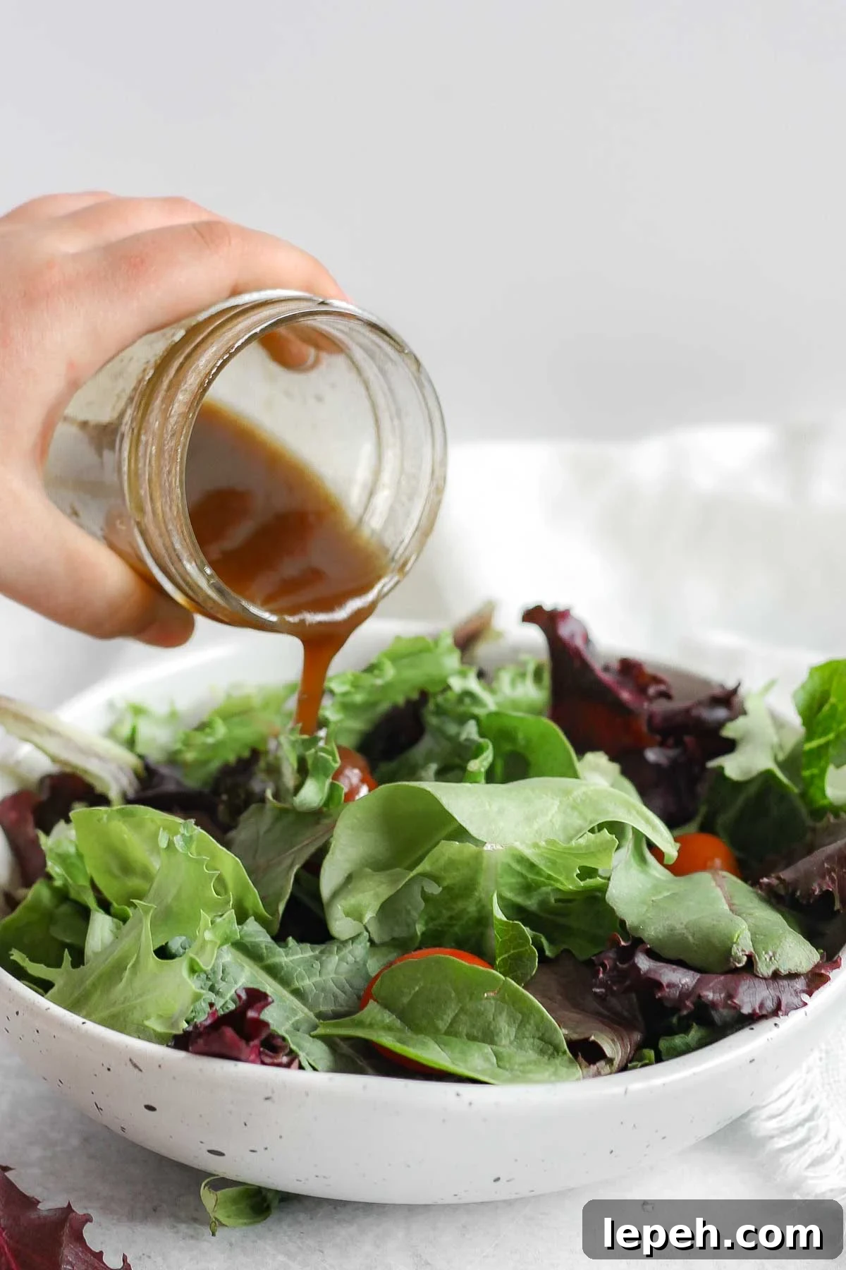 Balsamic vinaigrette being poured over a bowl of mixed greens.