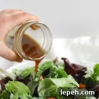 Balsamic vinaigrette being poured from a mason jar onto a bed of mixed greens.