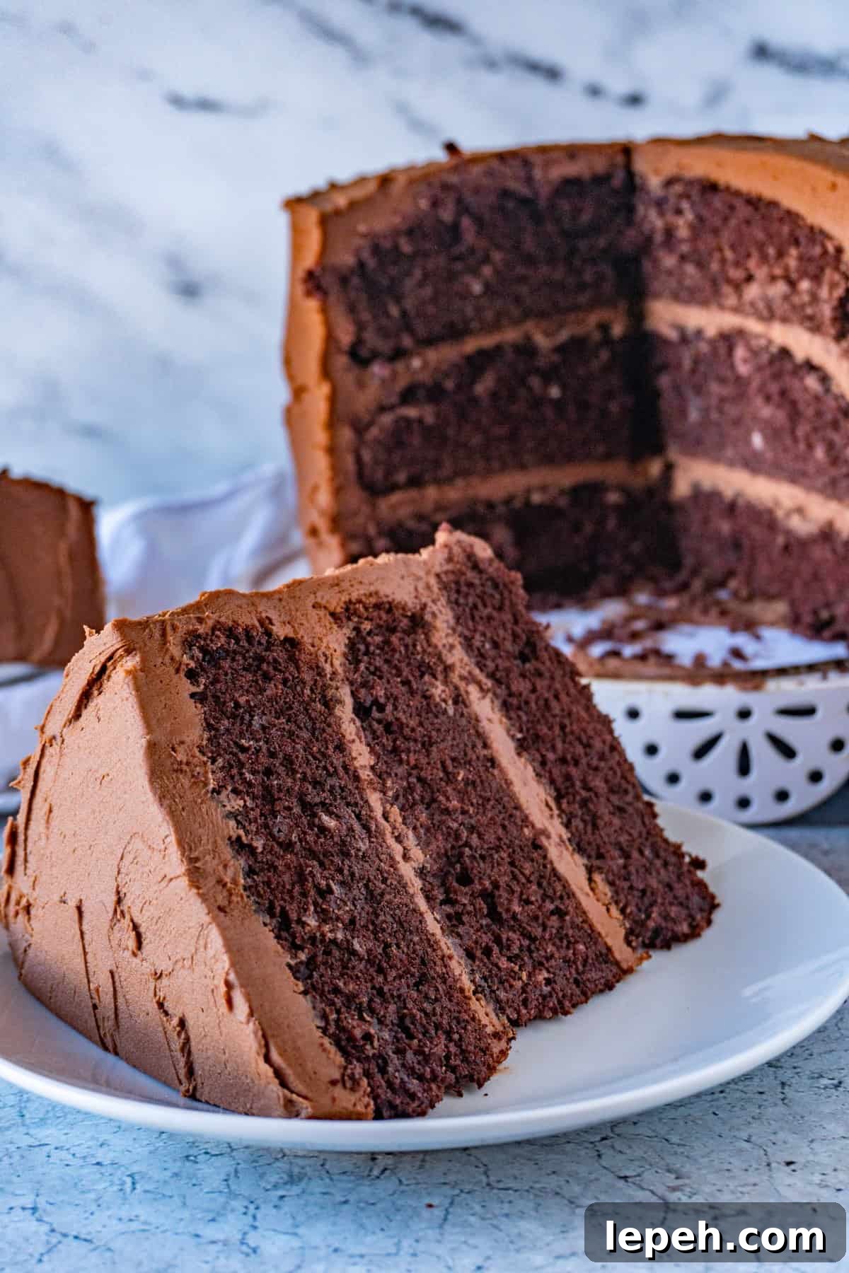 buttermilk chocolate cake slice with 3 layer son white plate and cut into cake in the background. 