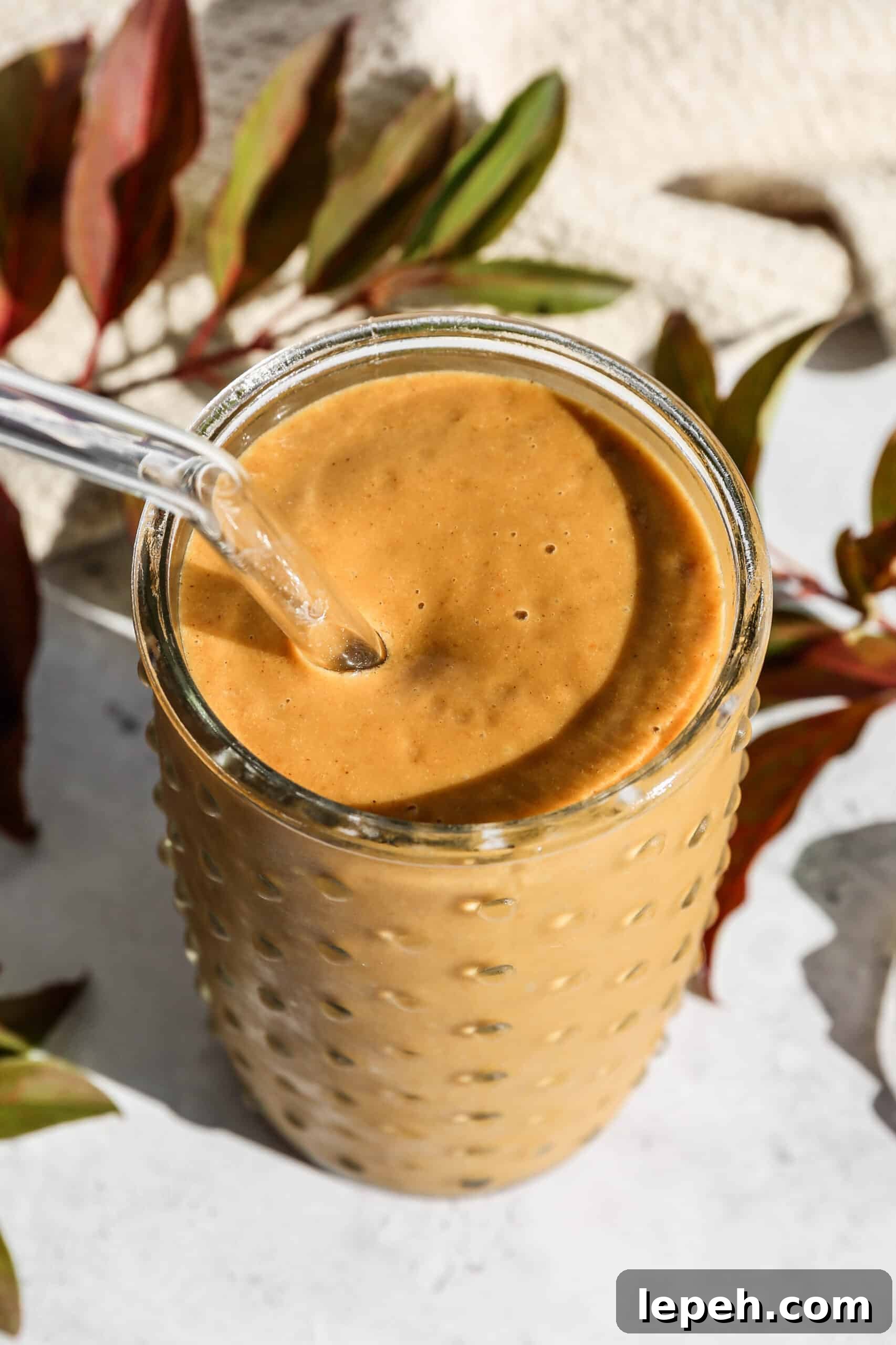 a glass of dairy free pumpkin pie smoothie with a glass straw next to some fall colored leaves.