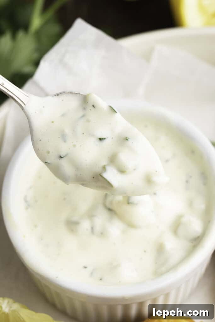 Vegan tartar sauce being lifted out of a small white ramekin on a silver spoon.