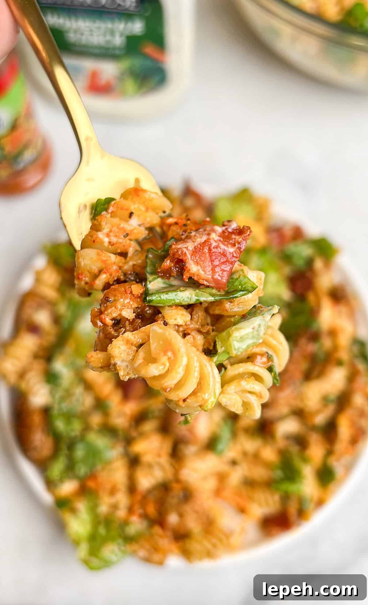 A forkful of chicken bacon ranch pasta salad above a bowl