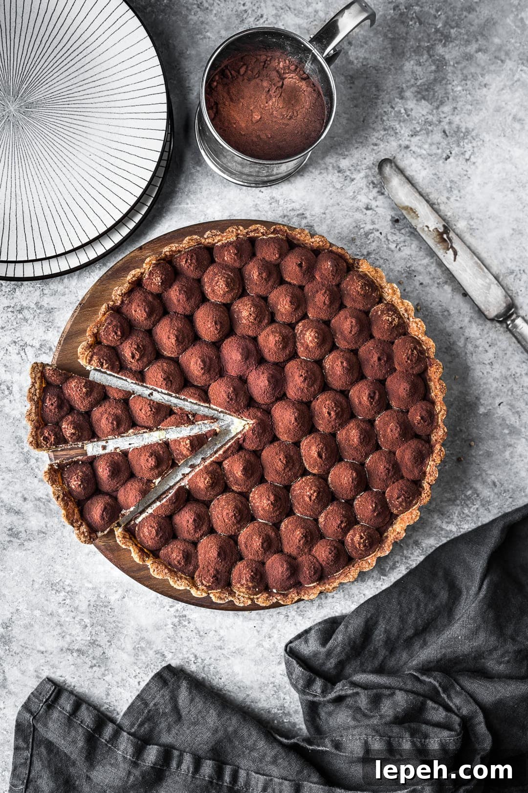 Tart with two slices cut, on a grey background with napkin and plates nearby