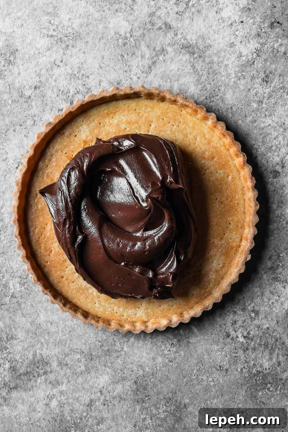 A blind baked tart shell with a chocolate mascarpone ganache filling before being spread.