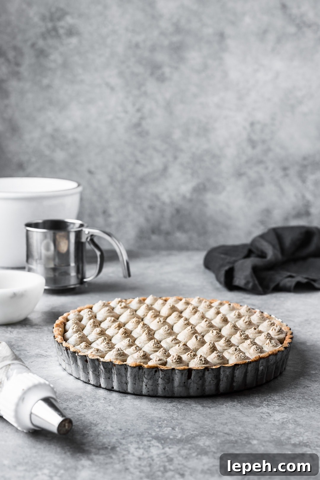 Tart resting on a grey background with bowls and piping bag nearby