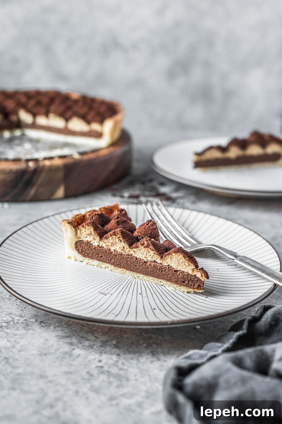 Slice of tart on plate on a grey background with rest of tart in background