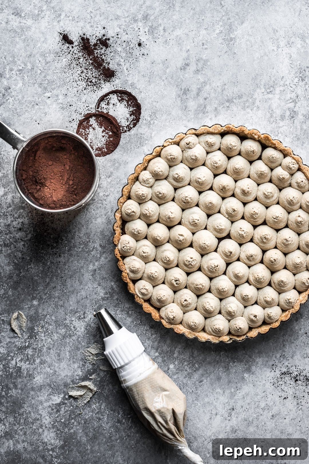 Chocolate coffee mascarpone tart on a grey background with cocoa powder and piping bag nearby