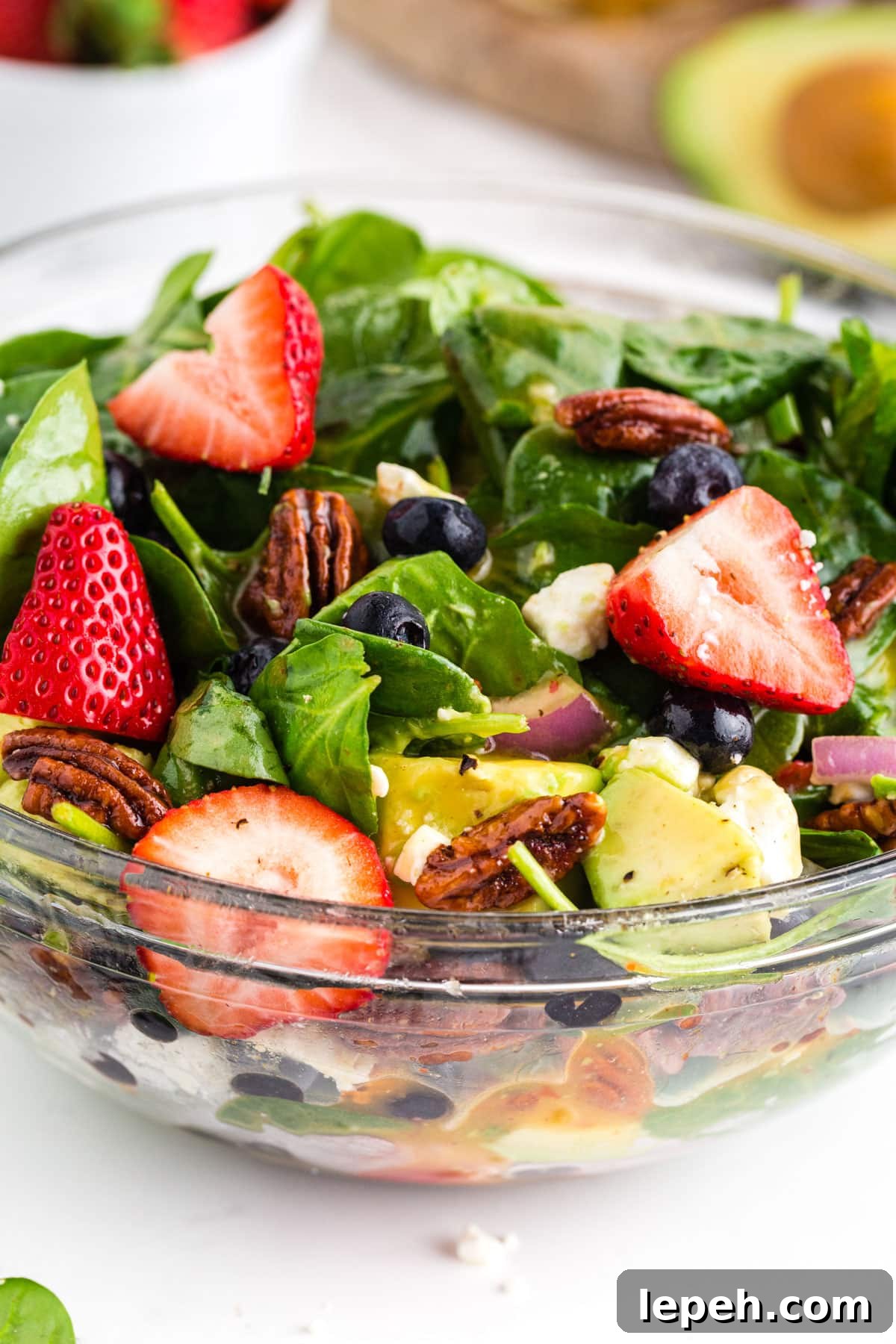 Strawberries, feta cheese, candied pecans, spinach, and avocado piled high in glass serving bowl.