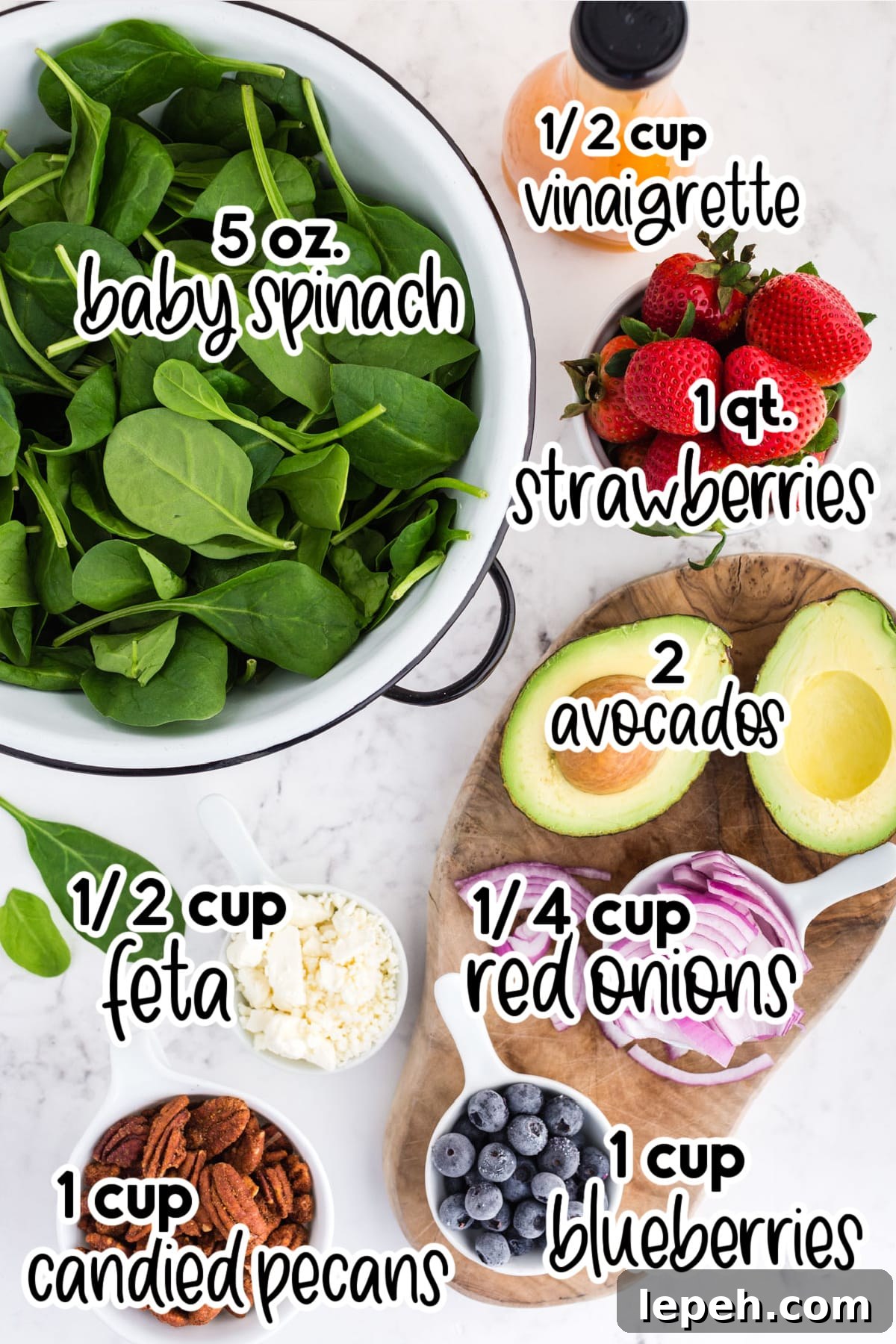Individual ingredients for strawberry feta spinach salad: baby spinach, vinaigrette bottle, strawberries, avocado, sliced red onions, feta cheese, blueberries, and pecans - with text labels.