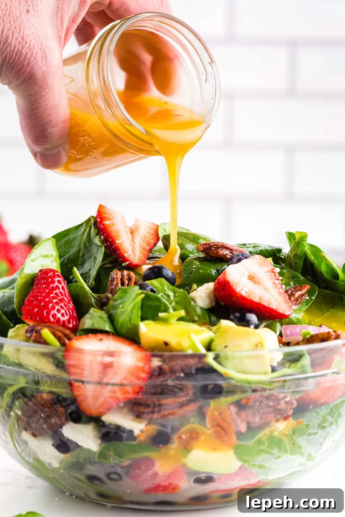 Salad dressing getting poured into a glass bowl filled with Strawberry Feta Spinach Salad.
