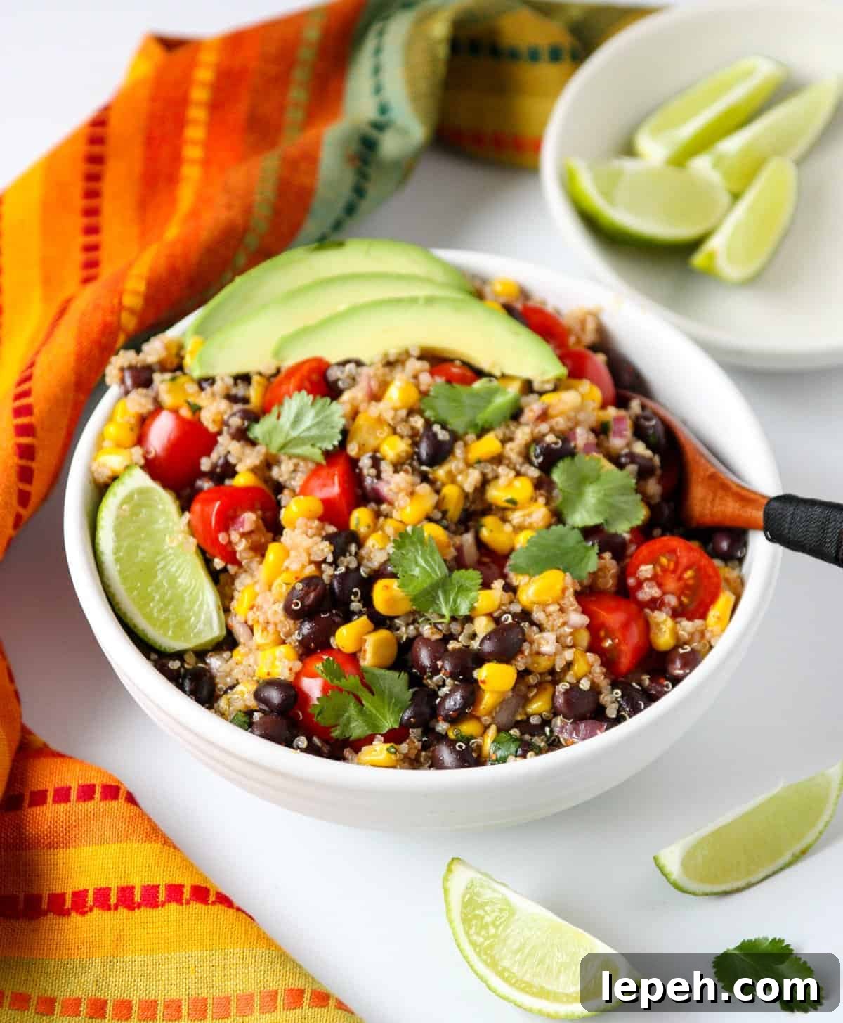 A bowl of Southwestern Quinoa Salad topped with avocado slices with a wooden fork.