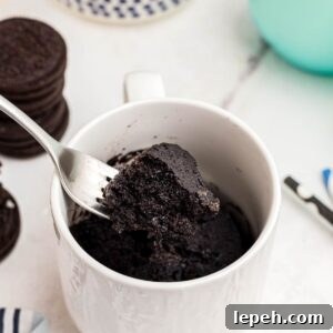 Chocolate mug cake with a bite scooped out on a fork with Oreos and milk on the table.