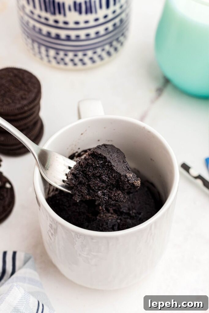 Scoop of chocolate cake being taken out of the mug on a fork with Oreos and glasses of milk on the table. 