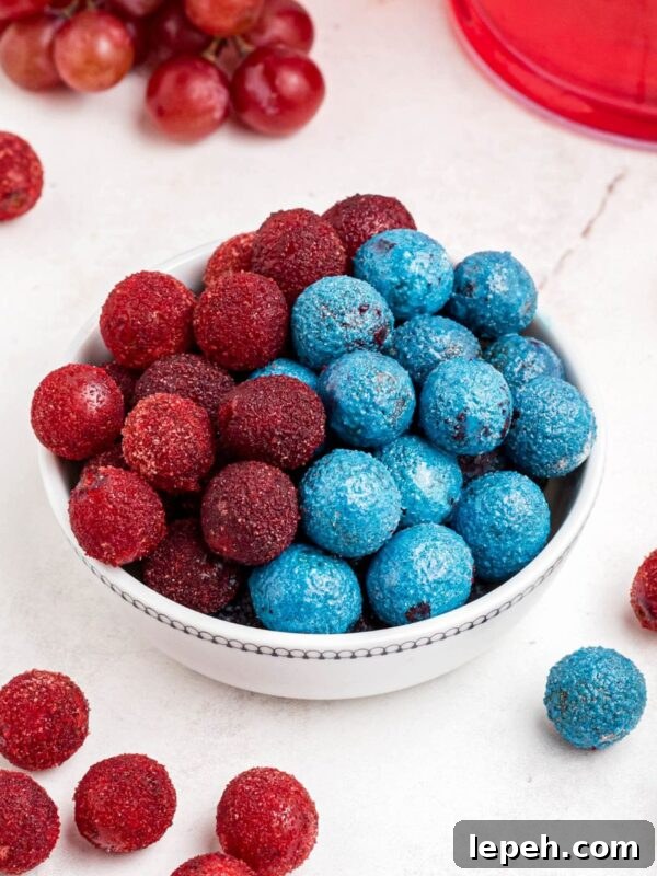 Red and blue candy grapes stacked in a white bowl with grapes scattered on a marble table.