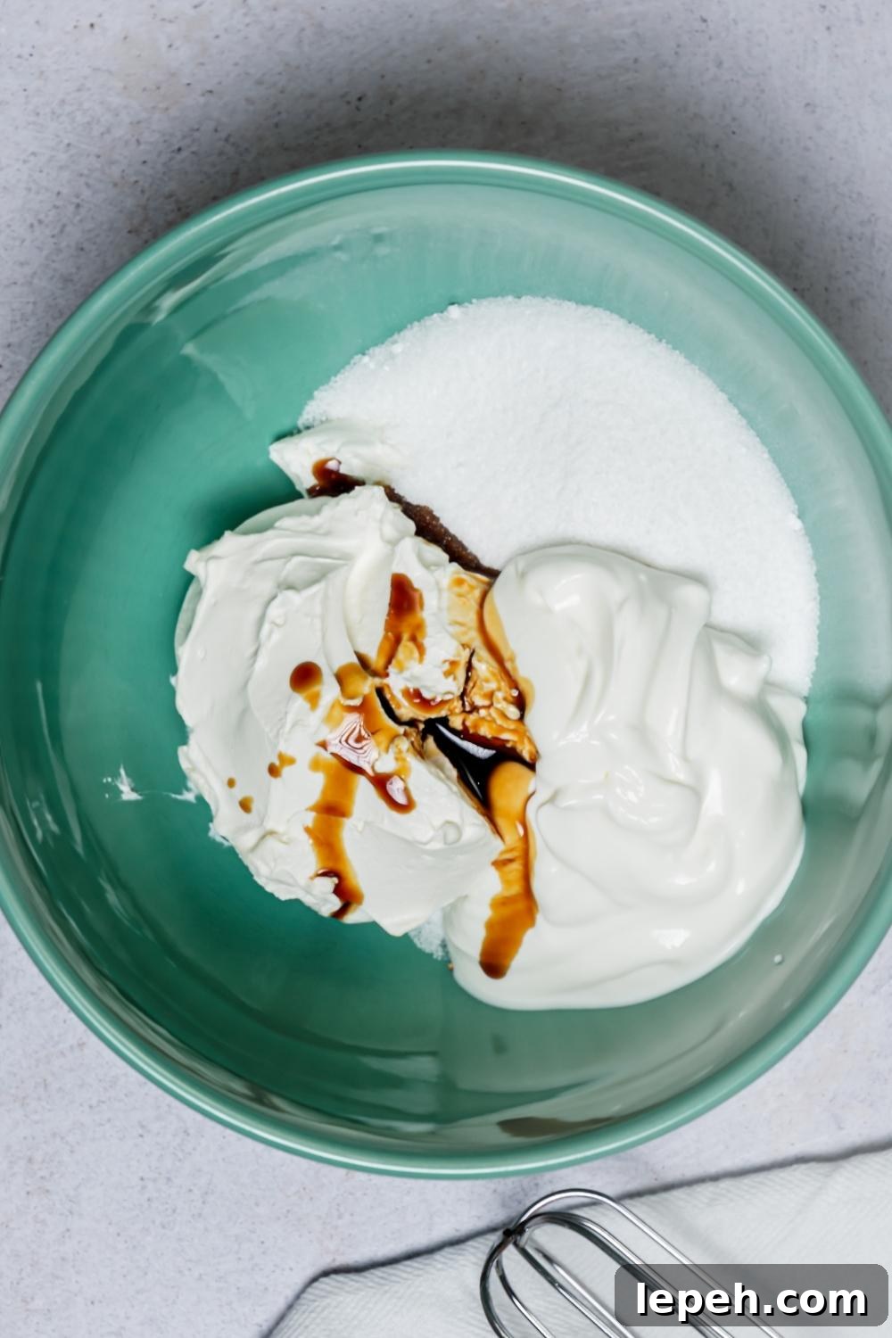 An overhead view of a mixing bowl with sour cream, sugar, vanilla, and room temperature cream cheese.