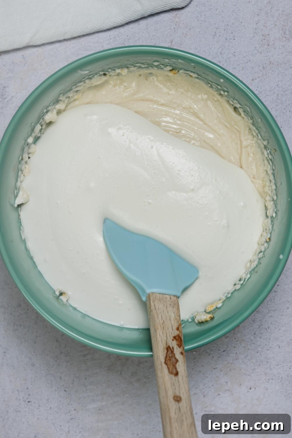 An overhead view of a mixing bowl with a creamy mixture of all the ingredients and cool whip on top. A rubber spatula sits in the bowl.