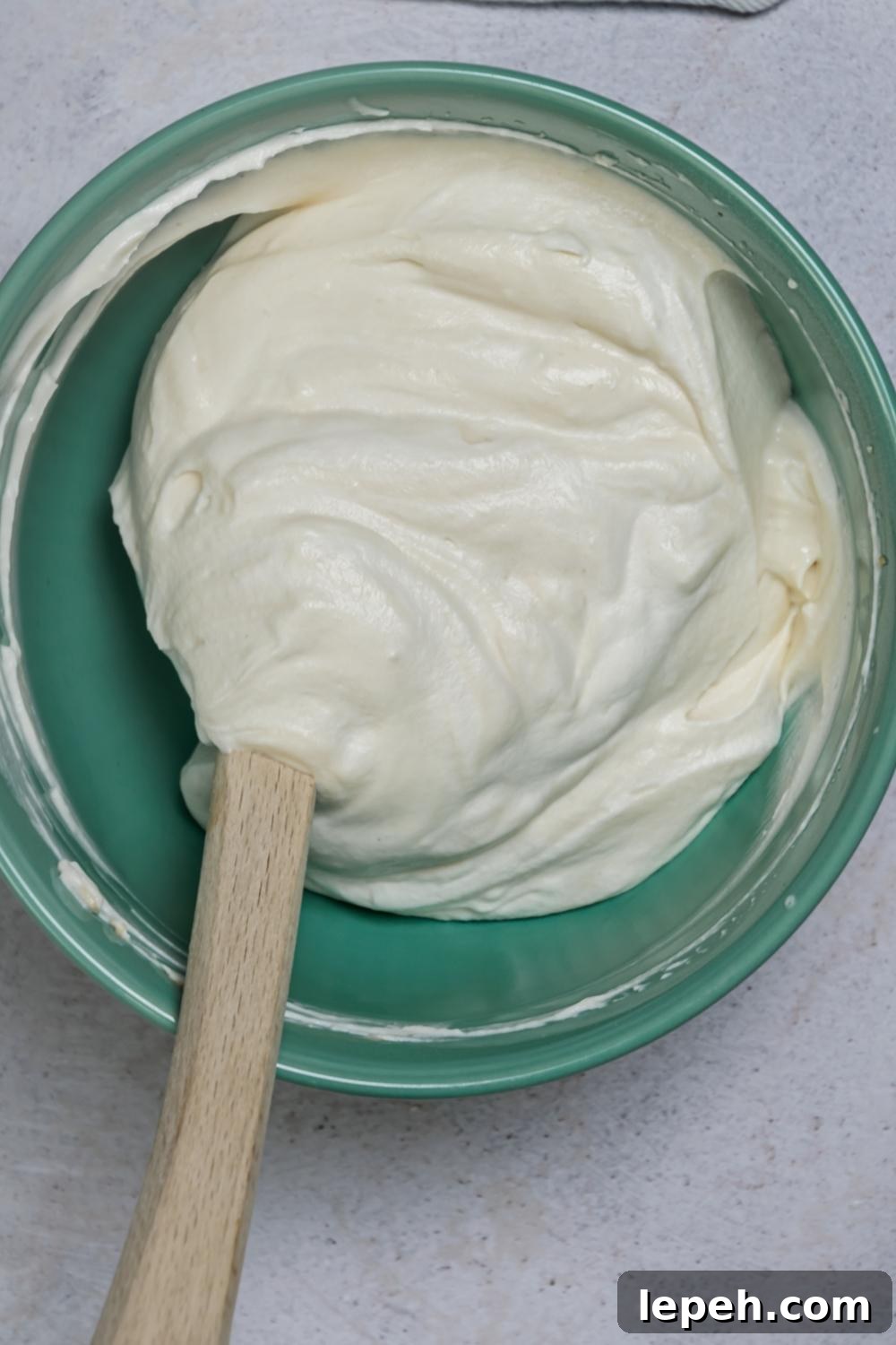 An overhead view of a mixing bowl with a creamy mixture of all the filling ingredients folded by a rubber spatula in the bowl.